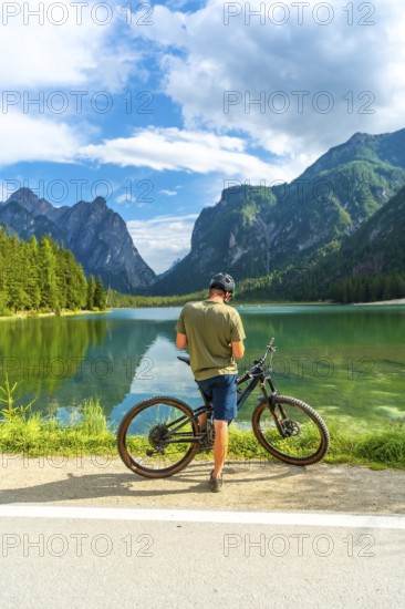 Mountain biker enjoying the breathtaking view of lake dobbiaco and the surrounding dolomites peaks on a sunny summer day