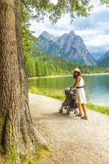 Tourist enjoying a walk with a baby stroller along the scenic shores of lake dobbiaco, surrounded by the stunning peaks of the dolomites