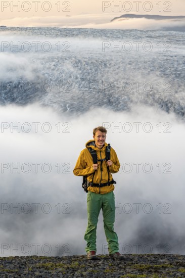 Young man in front of impressive landscape at sunset, fog, clouds moving around, glacier ice of the glacier tongue Kötlujökull, glacier Myrdalsjökull, Pakgil, Iceland