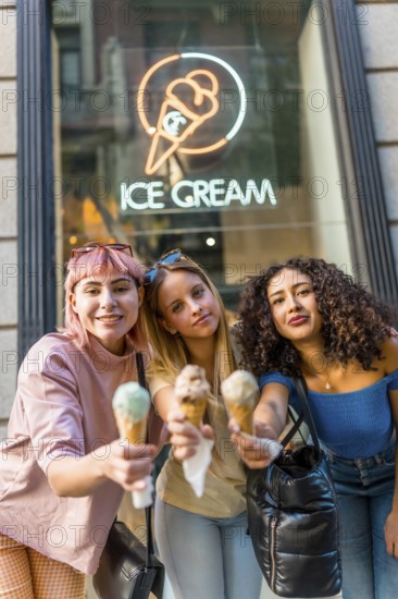 Vertical portrait of three diverse modern Women toasting with ice cream cones looking at camera in the street