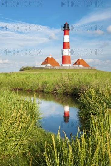 The Westerheversand lighthouse under a blue sky with white clouds reflected in a tideway, Westerhever, Eiderstedt peninsula, Schleswig-Holstein, Germany