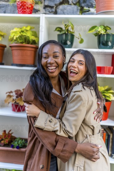 Two female shop assistants laughing and hugging each other in a plant shop, celebrating their friendship and teamwork