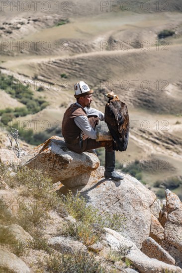 Traditional Kyrgyz eagle hunter hunting in the mountains in a dry landscape, near Kysyl-Suu, Issyk Kul, Kyrgyzstan