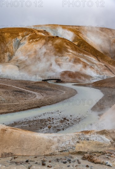 Bridge and steaming streams between colourful rhyolite mountains and snowfields, Hveradalir geothermal area, Kerlingarfjöll, Icelandic Highlands, Iceland