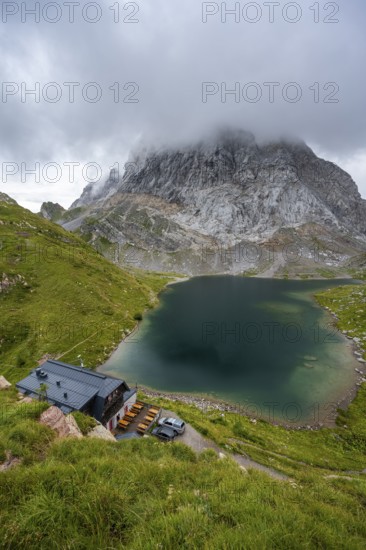 Alpenverinshütte Wolayerseehütte on Lake Wolayersee, cloudy mountain landscape with green meadows and mountain lake, Carnic Alps, Carnic High Trail, Carinthia, Austria