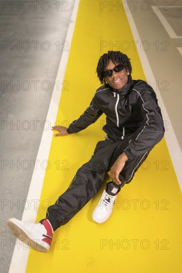 Vertical photo of an african modern musician sitting on the ground in an urban space