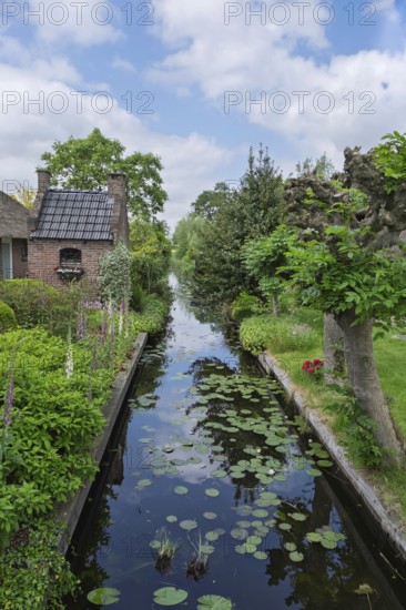Idyllic landscape with a canal between gardens and a brick house, surrounded by green vegetation and a blue sky, Giethoorn, municipality of Steenwijkerland, province of Overijssel, Netherlands