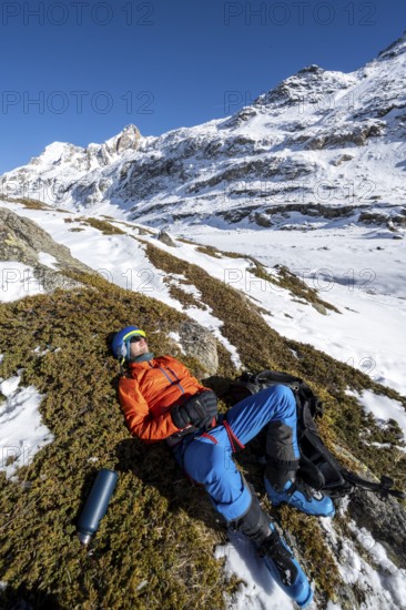 Ski tourer taking a break in the sun, lying down, taking a nap, snowy mountain landscape in winter, Ortler Alps, Vinschgau Valley, Italy