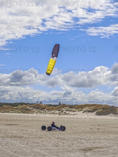 Recreational sport Beach kiting on the edge of the national park and UNESCO World Heritage Site, designated kite area, kite buggy steered with both feet, driver's seat with kiter between rear axle and front wheel, high speed, westerly winds, dunes on the beach, sunshine and blue sky, Sankt Peter-Ording, Schleswig-Holstein, Germany