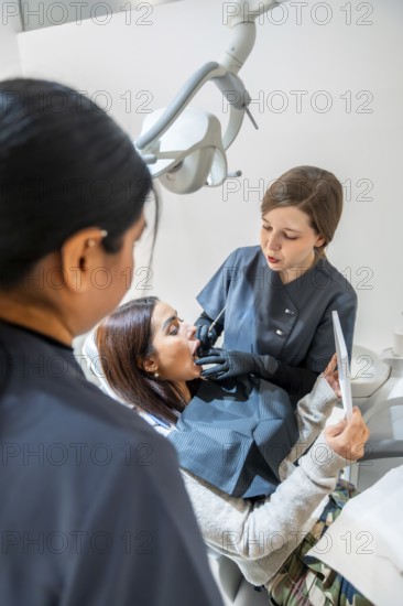 Dentist examining patient's teeth with dental tools while a nurse assists in a bright, modern dental clinic