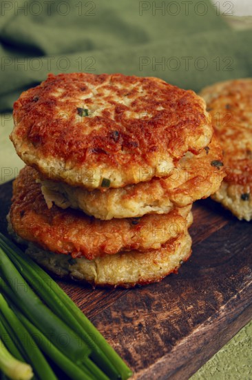 Crispy potato pancakes Latkes, stacked on a wooden board next to fresh green onions, natural light, homemade, no people