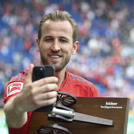 Harry Kane FC Bayern Munich FCB (09) smiles, proudly takes selfie with smartphone of his goal scorer's crown, honour, trophy, of the magazine Kicker Deutschland, PreZero Arena, Sinsheim, Baden-Württemberg, Germany