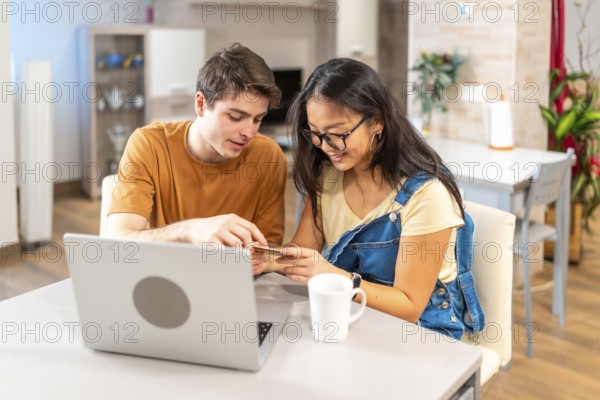 Young multiethnic couple using a credit card and a laptop to make an online purchase from their home
