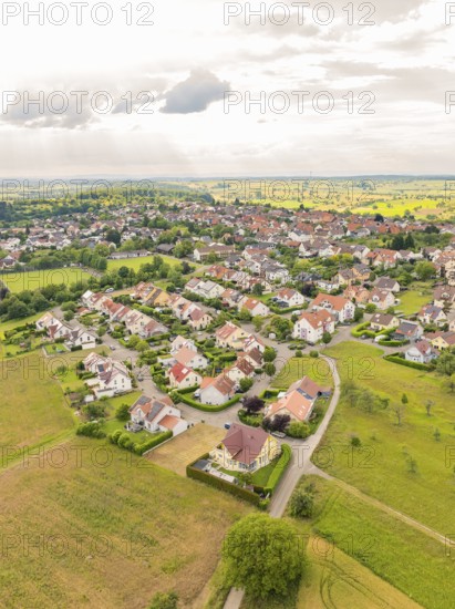 Residential area with densely built houses and streets, surrounded by fields under a slightly cloudy sky, Kieselbronn, Germany