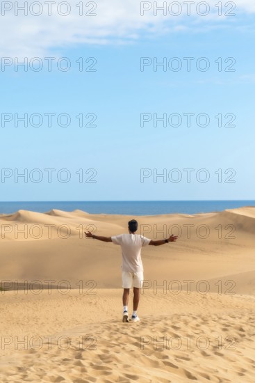 Young man opening arms in maspalomas dunes, gran canaria, feeling freedom and enjoying the desert landscape