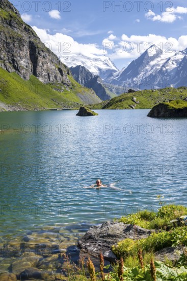 Woman bathing in mountain lake Lac de Louvie, behind summit of Grand Combin, Val de Bagnes, Valais, Switzerland