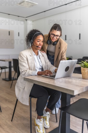 Two female customer service representatives collaborating on a laptop, providing assistance and solutions in a contemporary workspace