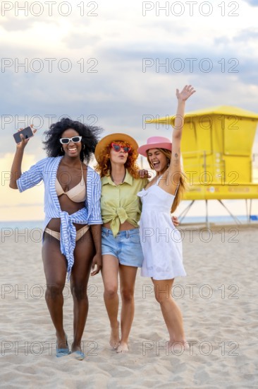 Three cheerful multiracial young women enjoying summer holidays on miami beach, laughing together under the sunny sky, soaking up the vibrant atmosphere