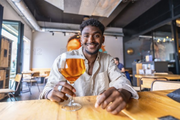 Happy customer is holding a glass of beer while sitting at a table in a modern and stylish restaurant