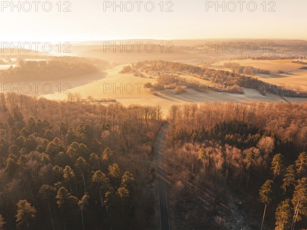 Aerial view of a road through a forest and past fields in the soft morning light, Gechingen district of Calw, Black Forest, Germany