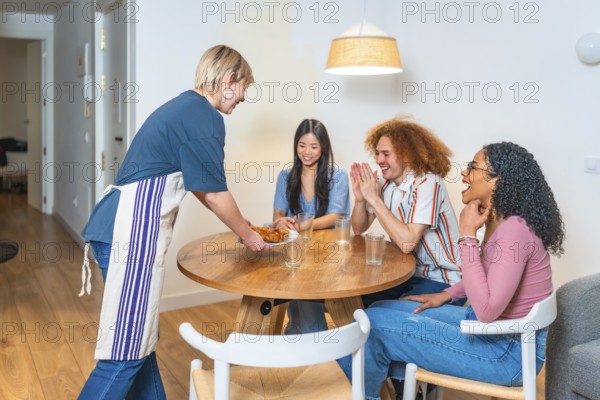 Happy multi ethnic friends are clapping hands while a woman is serving them food in a modern apartment