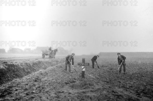 Wooden cross on grave of fallen soldier and workers levelling field on former battlefield after the First World War One in West Flanders, Belgium