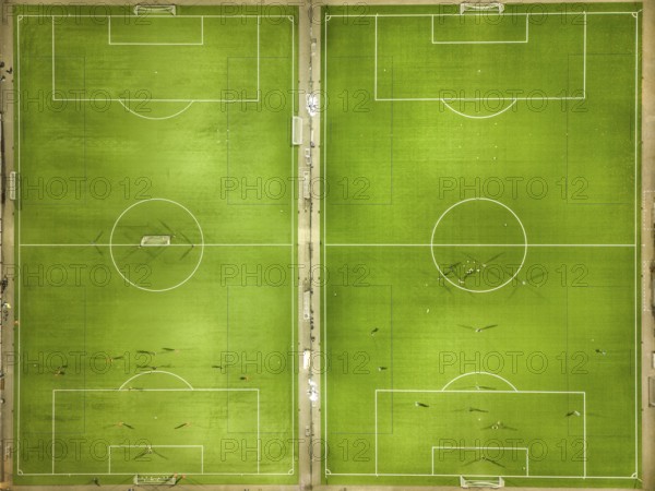Two symmetrical football pitches from a bird's eye view with scattered players on the green pitch