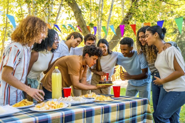 Young man celebrating birthday during picnic with multi-ethnic friends in a park