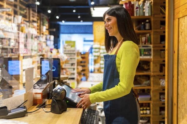 Smiling saleswoman using a digital checkout in an organic supermarket or grocery store, selling natural or gluten free products