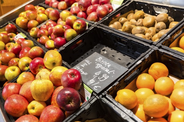 Fruit counter in a supermarket or organic food shop, here with different types of apples, kiwis, oranges and an empty compartment for pears