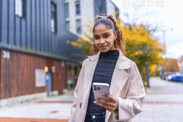 African smiling woman using cellphone walking along the city in autumn