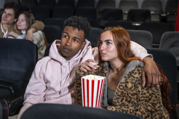 Young multi ethnic couple watching a movie in cinema, eating popcorn and enjoying their time together