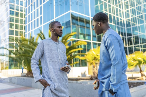 Two senegalese businessmen wearing traditional dashiki attire are discussing business in front of modern office buildings