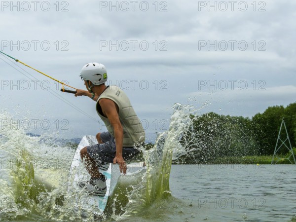 Young man jumping into the lake with a wakeboard, water sports, water skiing in the wake park