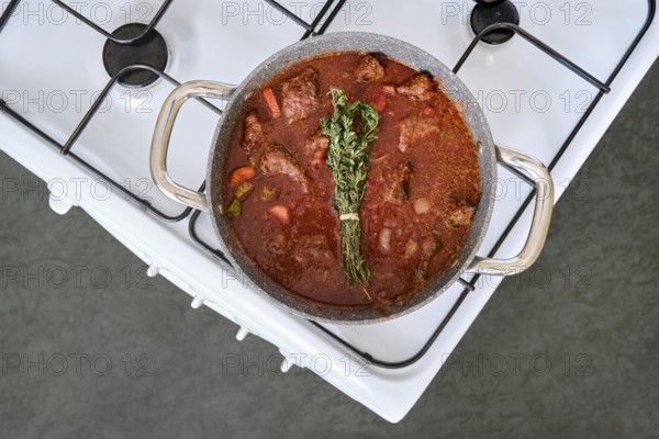A pot of beef stew is bubbling on a white stove, filled with tender meat, colorful vegetables, and fresh herbs. The rich aroma fills the kitchen, inviting warmth and comfort for dinner