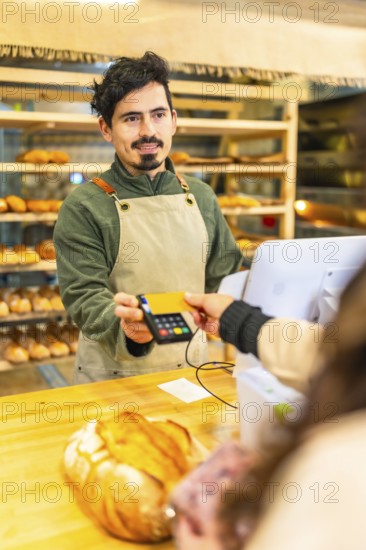 Vertical photo of a client paying with contact less credit card in a bakery