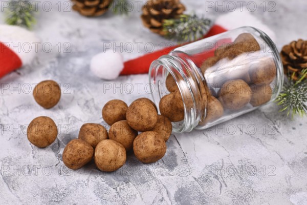Traditional German Christmas sweets called Marzipankartoffeln. Round ball shaped almond paste pieces covered in cinnamon and cocoa powder spilling out of glass jar surrounded by seasonal decoration