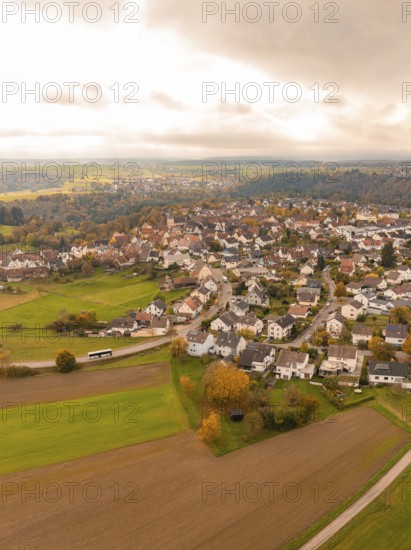 Aerial view of a village surrounded by autumnal fields under a cloudy sky, Tiefenbronn, Germany