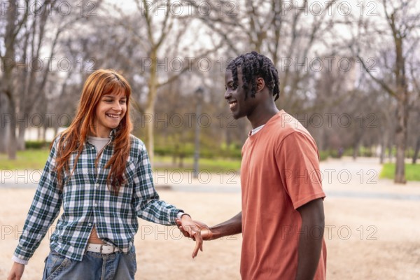 Young interracial couple holding hands and smiling while walking in a park, enjoying a romantic date outdoors