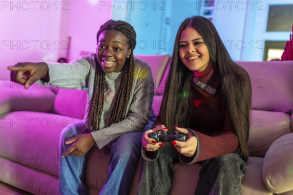 Two friends enjoying their free time playing video games at home, sitting on a comfortable sofa in a colorful living room