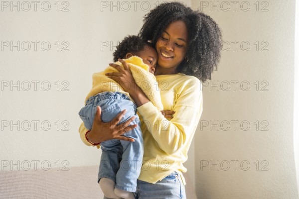 African mother holding her little daughter in arms standing at home
