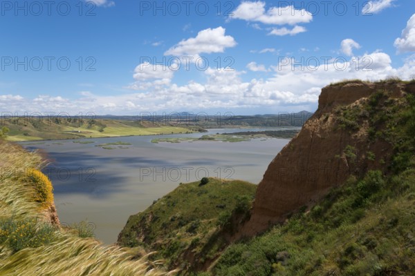 Ein weiter Blick auf einen See inmitten einer hügeligen Landschaft unter einem blauen, wolkigen Himmel, Barrancas de Burujón, Burujon, río Tajo, Fluss Tajo, embalse de Castrejón, Stausee de Castrejon, Toledo, Kastilien-La Mancha, Spanien