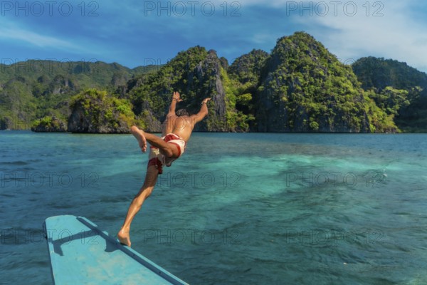 Young man diving from traditional bangka boat into the turquoise waters of coron island, philippines, enjoying summer holidays in southeast asia