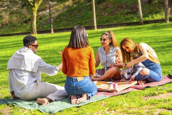 Group of diverse friends enjoying pizza and laughter during a sunny picnic in a vibrant park, creating joyful memories together