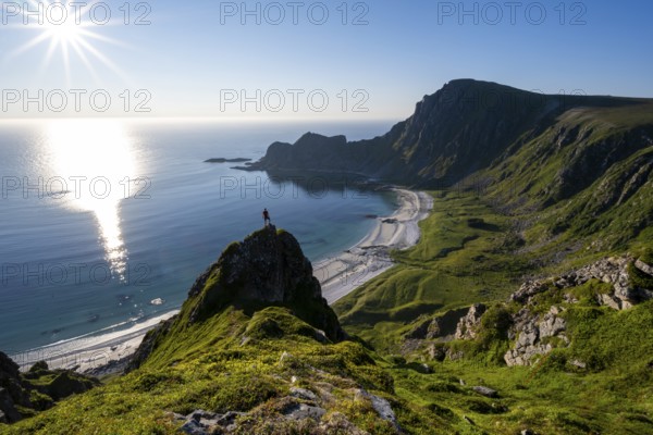 Climber on a rock, view of picturesque coastal landscape with sun star, steep coast with peak Måtind or Måtinden, Høyvika beach and sea, hike to the summit of Måtind, Andøya island, Vesterålen, Nordland, Norway