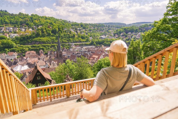A person sitting on a terrace with a view of a town and the surrounding hills, Panorama Holzsteg, Calw, Black Forest, Germany