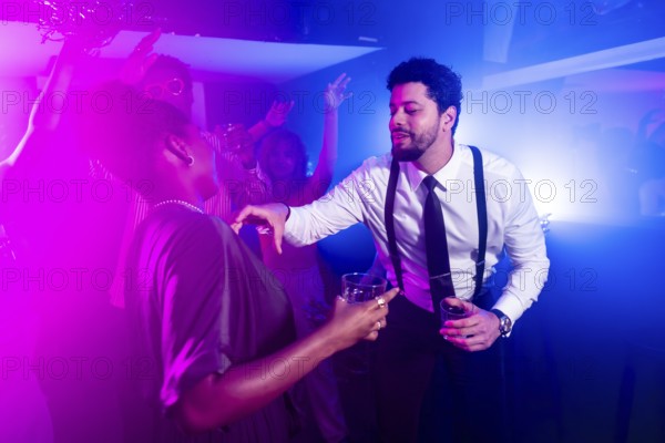 Businessman flirting with beautiful woman while holding alcoholic beverages and dancing at nightclub party with friends in background