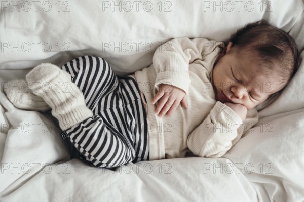 Sleeping baby in a striped romper lying on a white bed, looks peaceful and secure