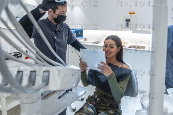 Dentist showing dental scan results on a tablet to smiling patient, in a modern dental clinic
