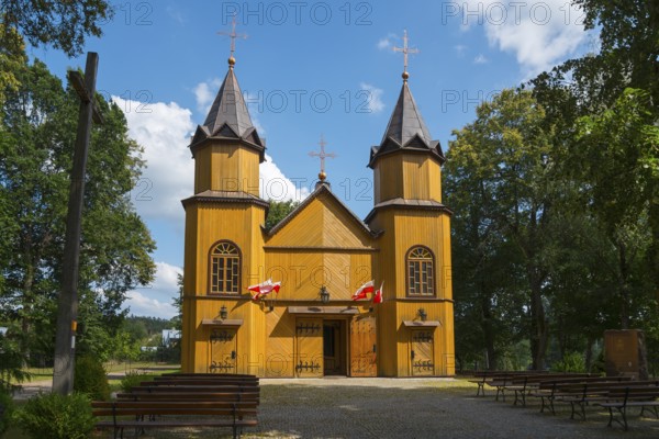 Wooden church with two towers, surrounded by trees and under a blue sky in the sunshine, wooden church of St Mary Magdalene, Mikaszówka, Mikaszowka, Powiat Augustowski, Podlaskie Voivodeship, Poland